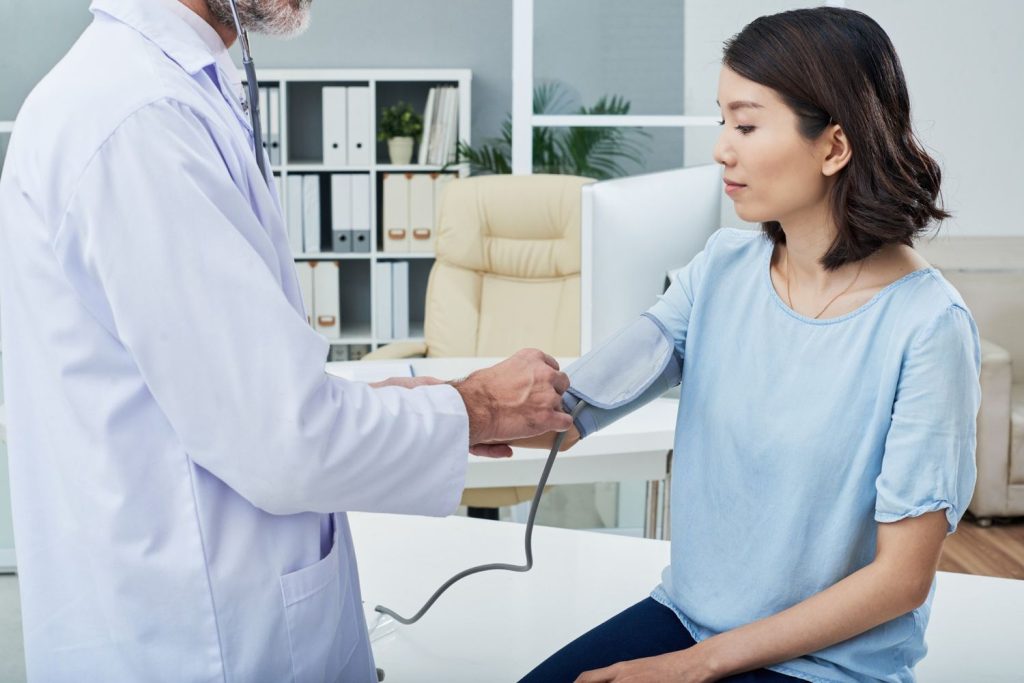 Doctor checking blood pressure for an immigration medical physical, ensuring patient health in a clean office.