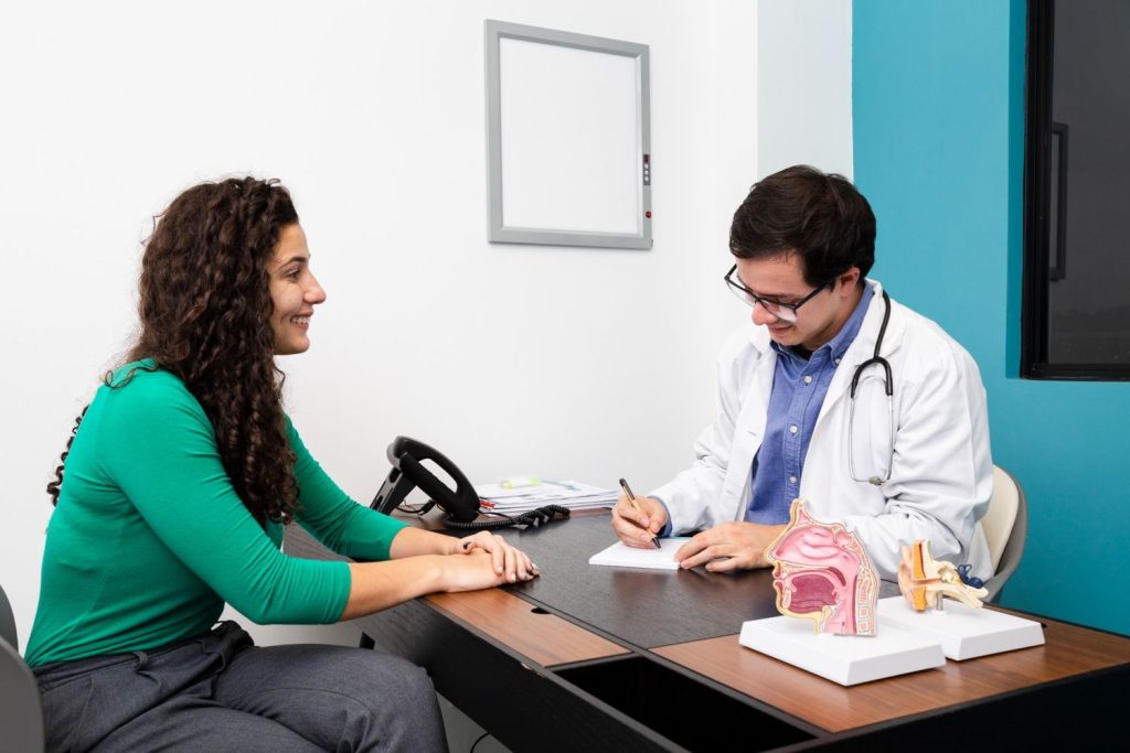 Doctor taking notes during an immigration medical physical, with patient and anatomical models on the desk.