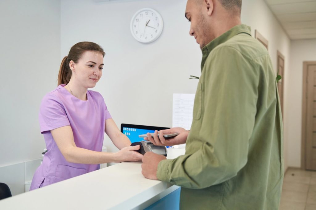 Patient makes card payment at front desk after USCIS immigration medical exam at Houston medical facility reception.