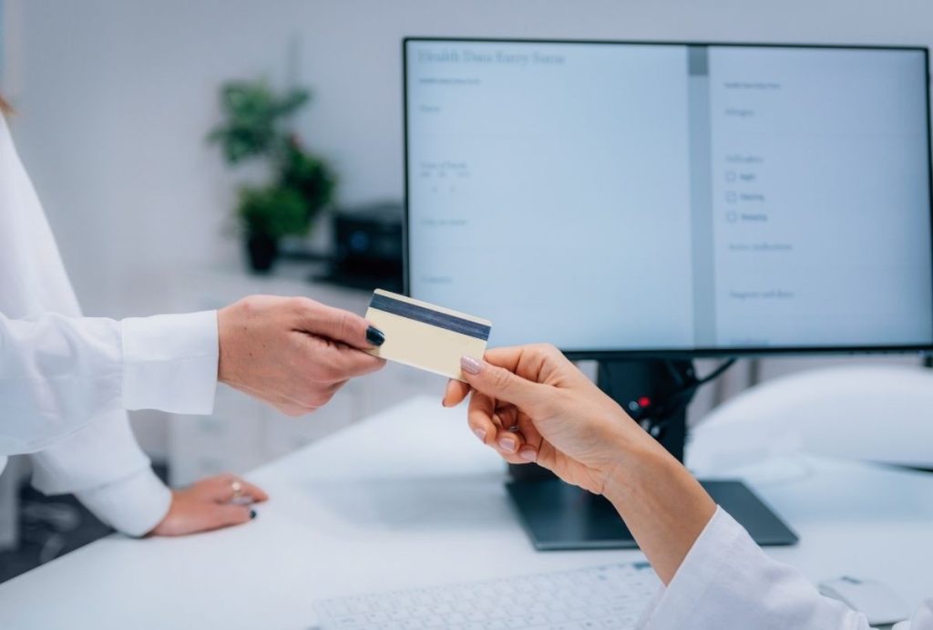 Patient handing insurance card to staff during USCIS immigration medical physical registration at Houston clinic front desk.