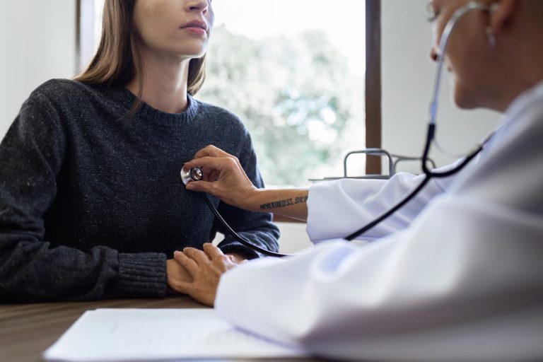 Female doctor using stethoscope during cheapest immigration medical exam Houston to check patient heart and lung function.