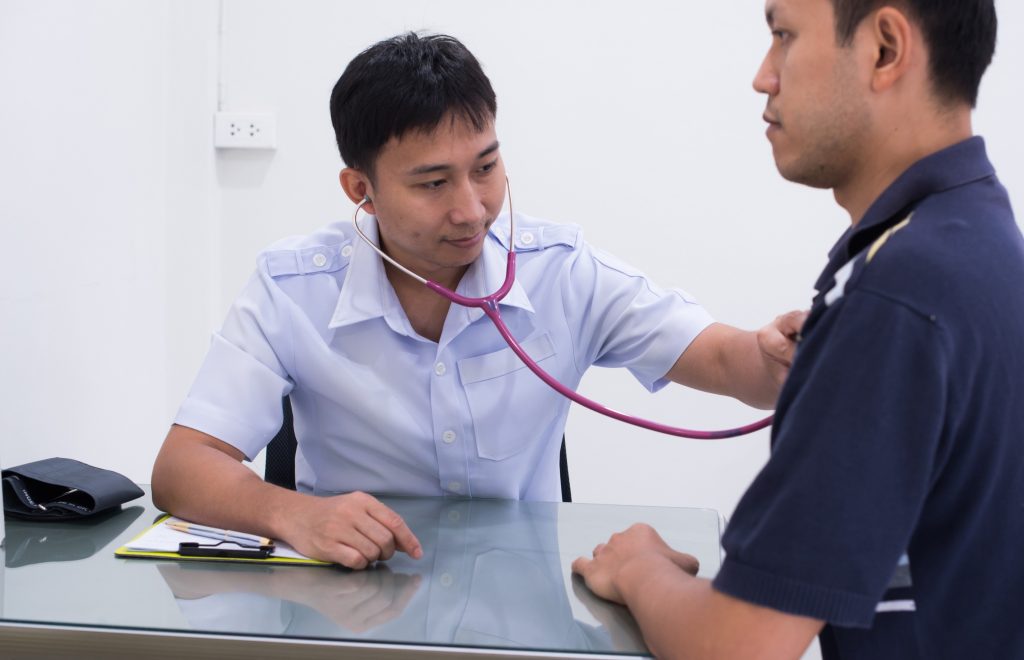 Male doctor conducting an immigration medical physical Houston exam using a stethoscope to check a patient's heart.