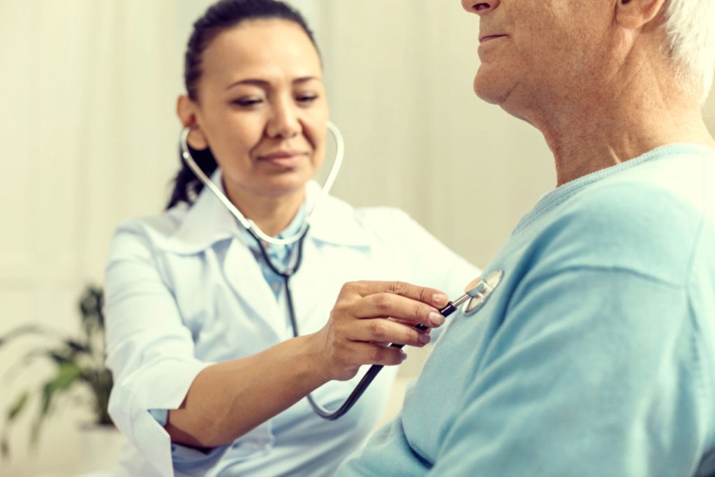 Immigration medical physical exam with doctor using stethoscope to check heart and lungs of senior patient in clinic setting