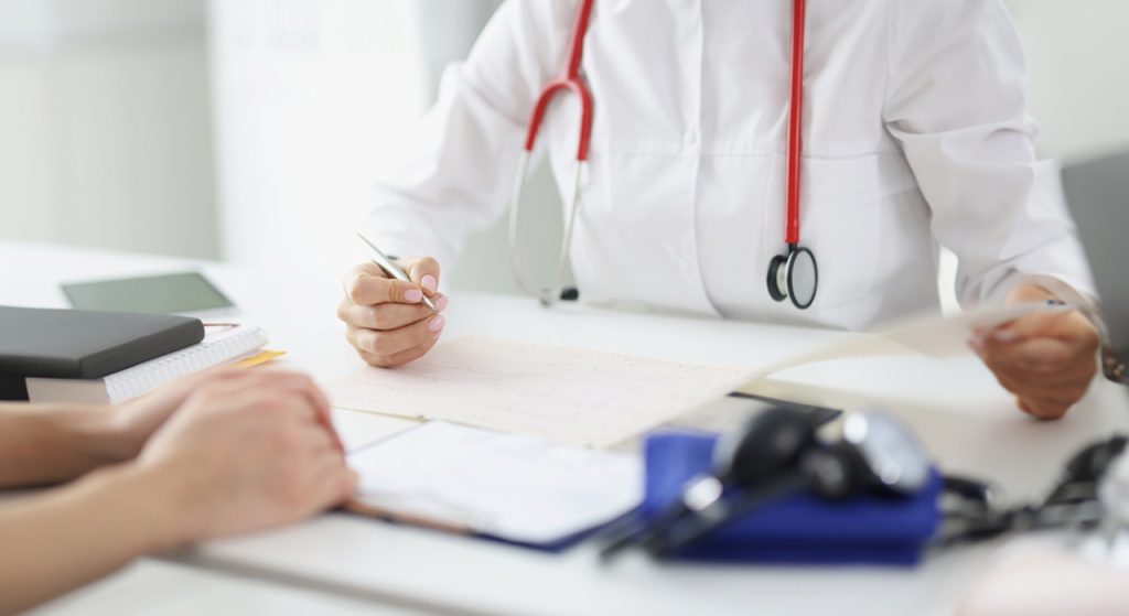 Close-up of a doctor with a stethoscope conducting an USCIS immigration medical exam at a clean, white clinic desk.