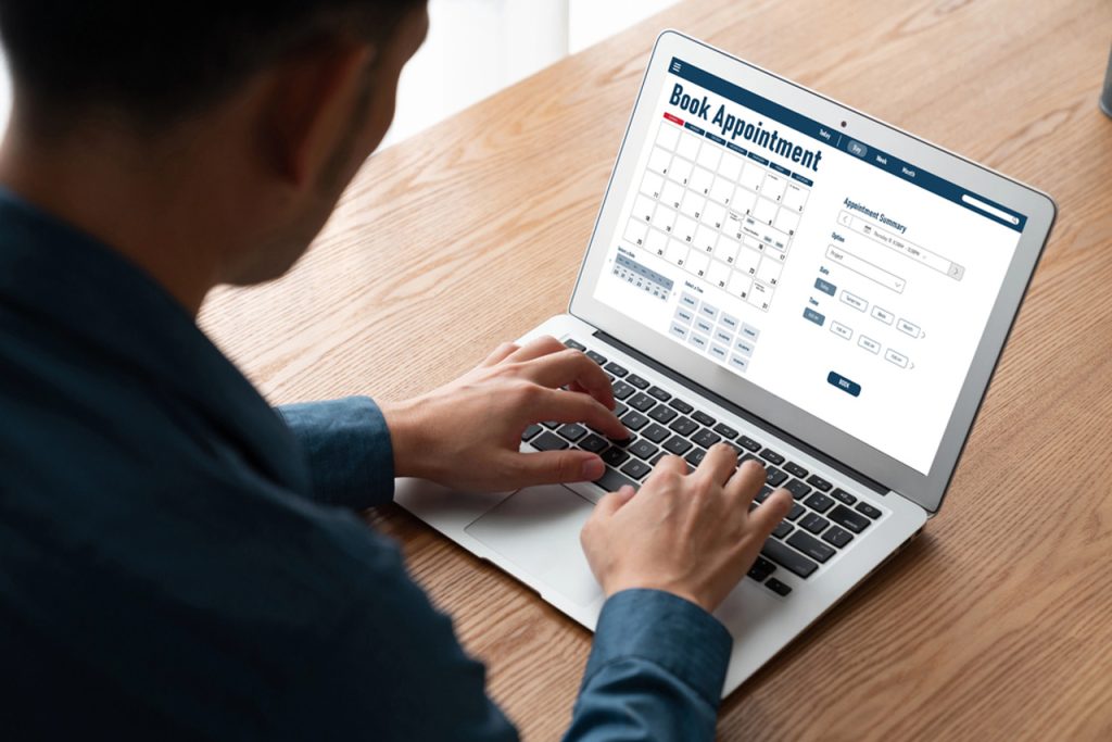 A person uses a laptop to schedule their required USCIS immigration medical physical exam on an online calendar.
