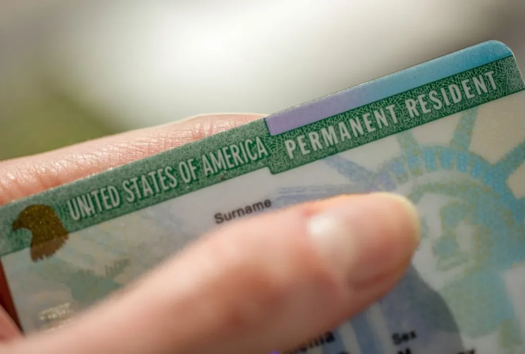 A close-up of a hand holding a US permanent resident green card, a required step in the green card medical exam process.