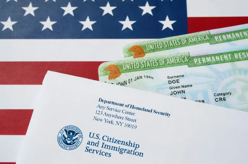 US permanent resident green cards and an official DHS envelope on an American flag, showing the successful result of a green card medical exam.