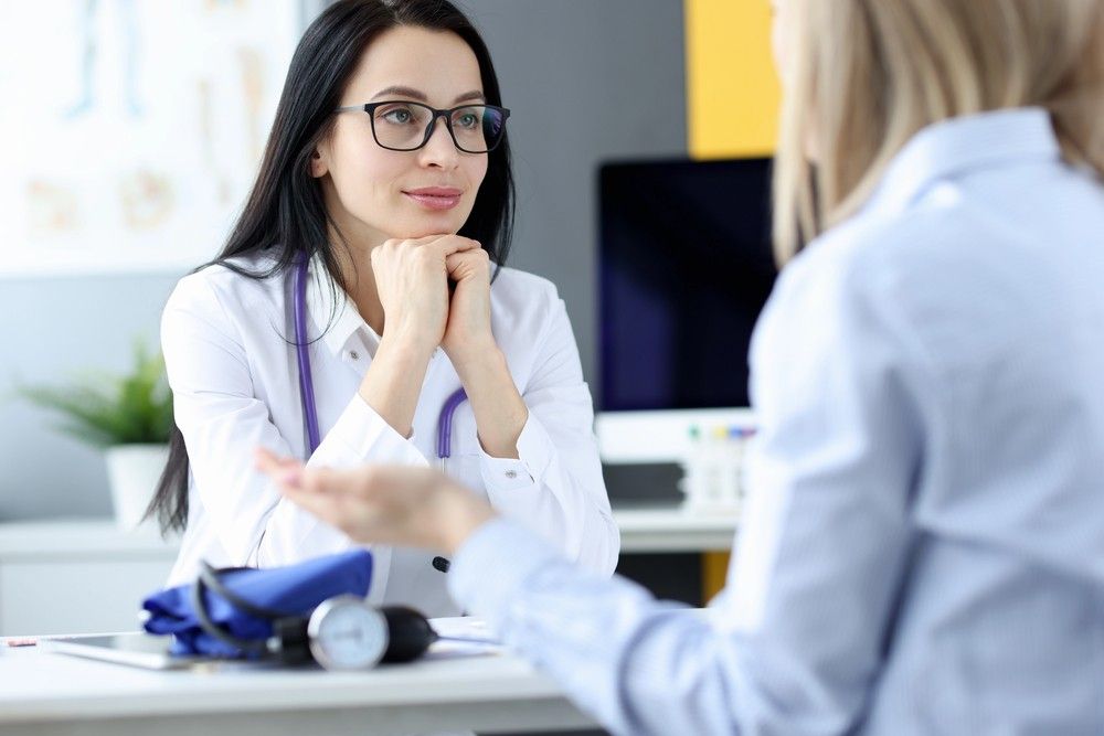 A brunette female immigration doctor Houston medical professional listens to a patient next to a blood pressure cuff.