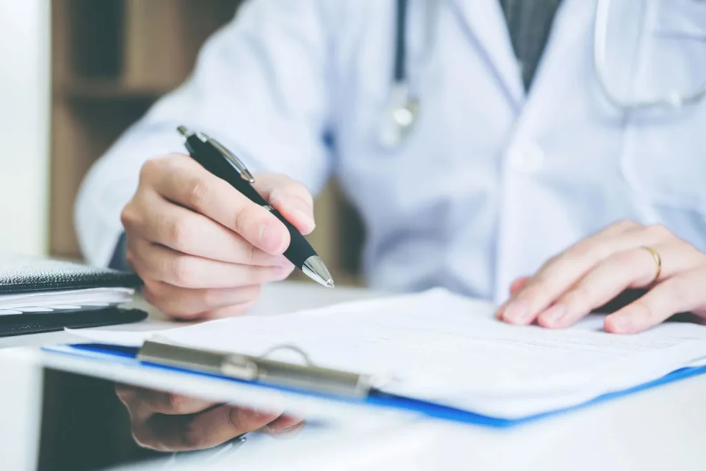 Close-up of a doctor’s hand filling out the official form after a completed USCIS immigration medical exam.