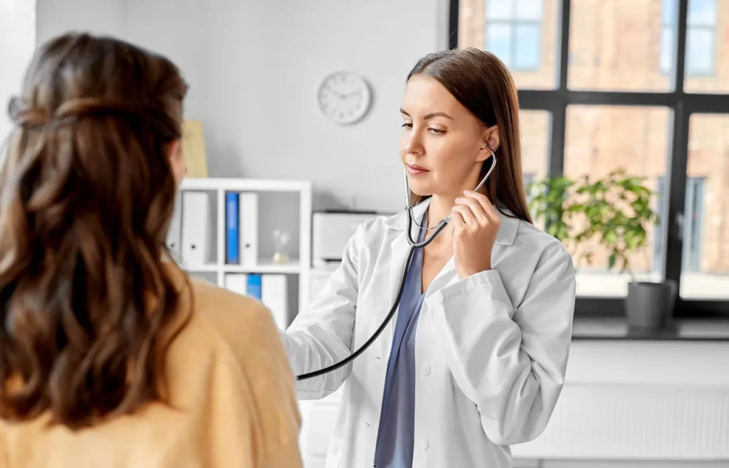 A female doctor checks a patient's lungs with a stethoscope at our immigration exam clinic open now Houston.
