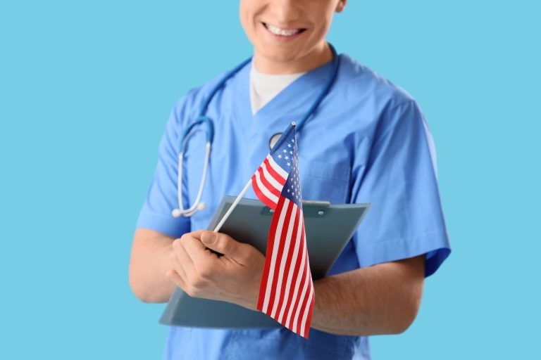 Smiling male medical provider in blue scrubs holding a US flag, ready to assist as a USCIS approved doctor Houston.