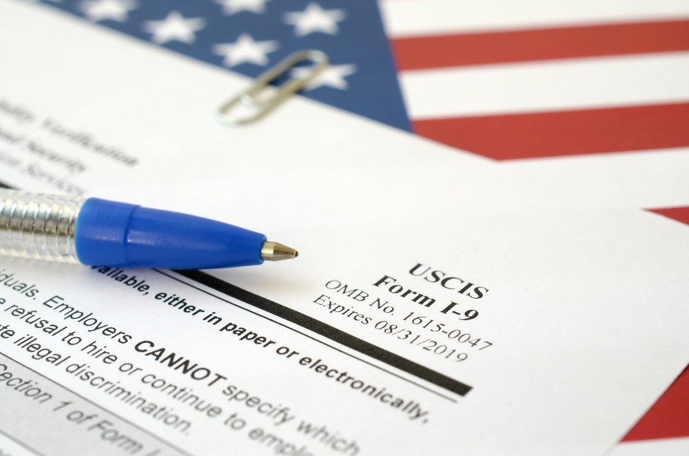 USCIS Form I-9 with a blue pen and American flag background, part of the process for the cheapest immigration medical exam Houston.