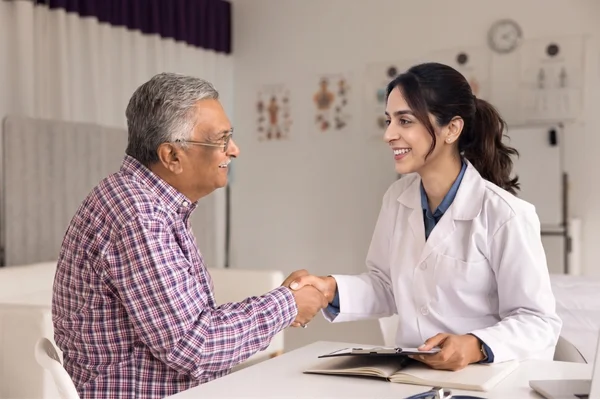 Female doctor shaking hands with a senior patient during an immigration medical exam.
